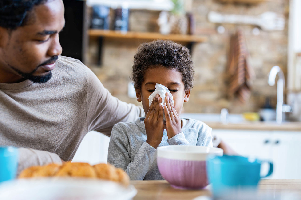 Father and child. Child is blowing his nose.